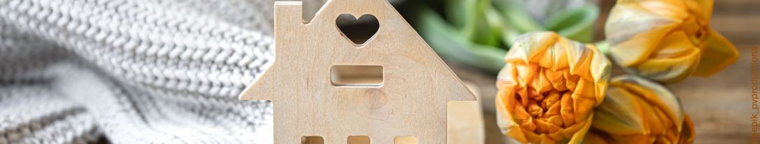 Holzschlablone einer Hausfassade mittig, links weißer Wollschal, rechts Tulpen in orange